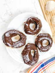 A white plate with four chocolate glazed donuts.
