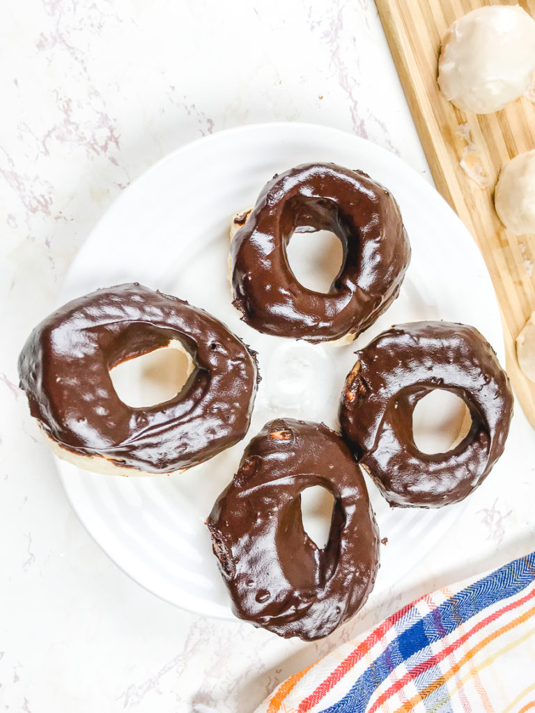 A white plate with four chocolate glazed donuts.