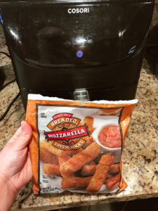 Bag of mozzarella sticks being held in front of black air fryer.