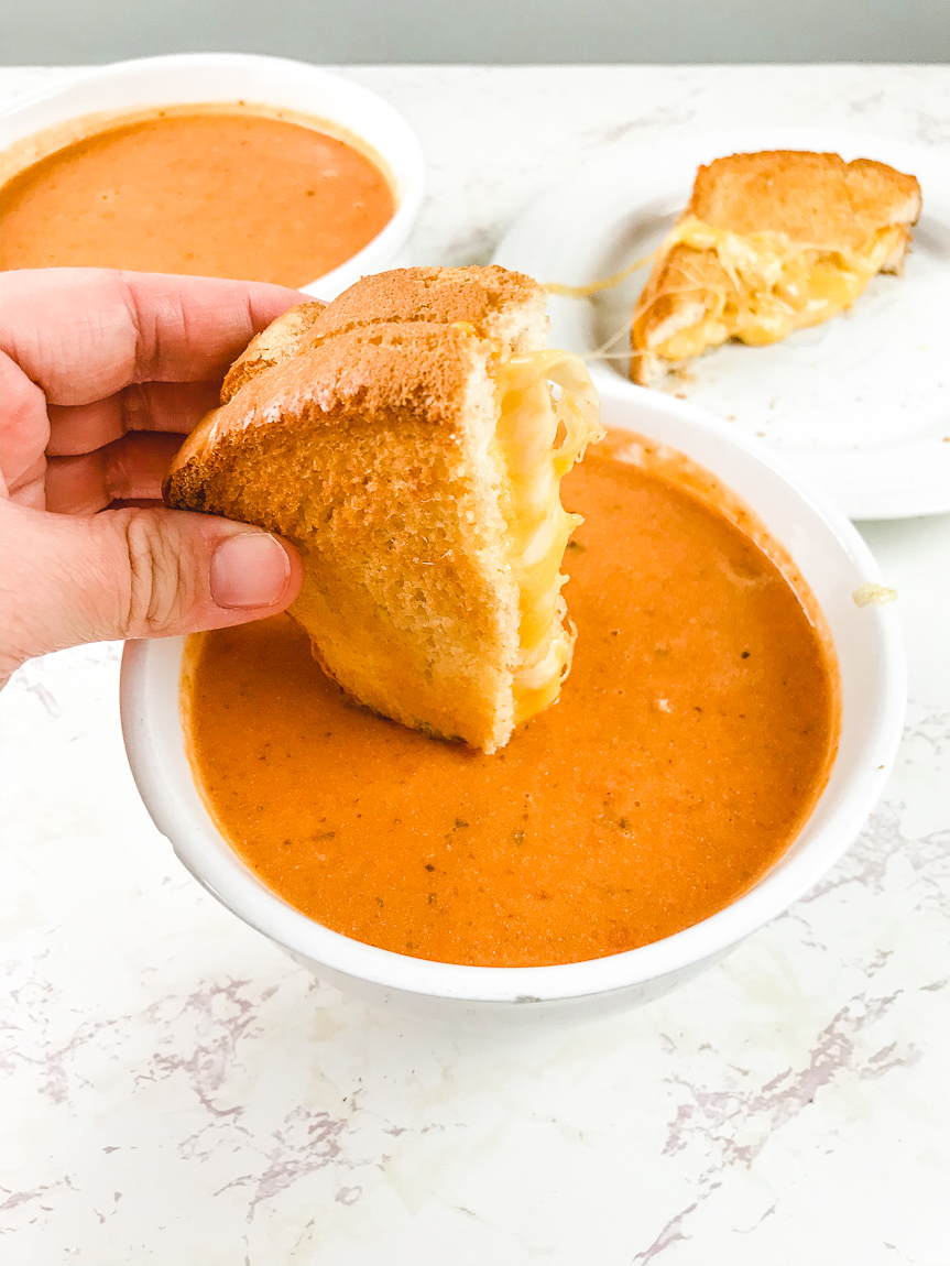 A grilled cheese being dipped into a bowl of tomato soup.