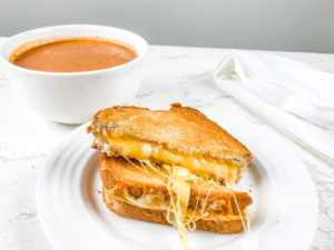 A grilled cheese on a white plate next to a bowl of tomato soup.