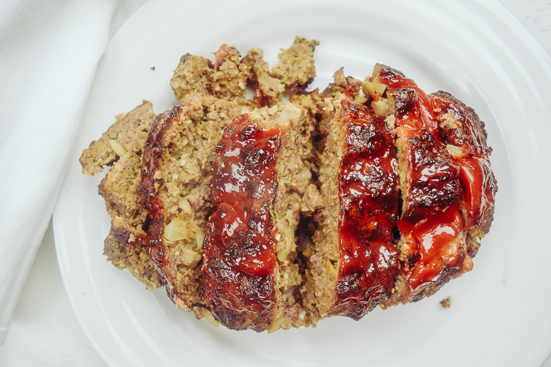 Sliced meatloaf topped with ketchup on a white plate.