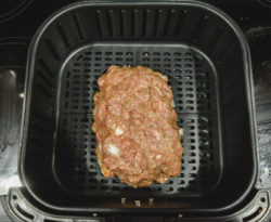 Raw meatloaf inside basket of air fryer.