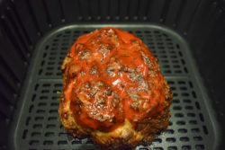 Cooked meatloaf with ketchup brushed on top inside air fryer basket.