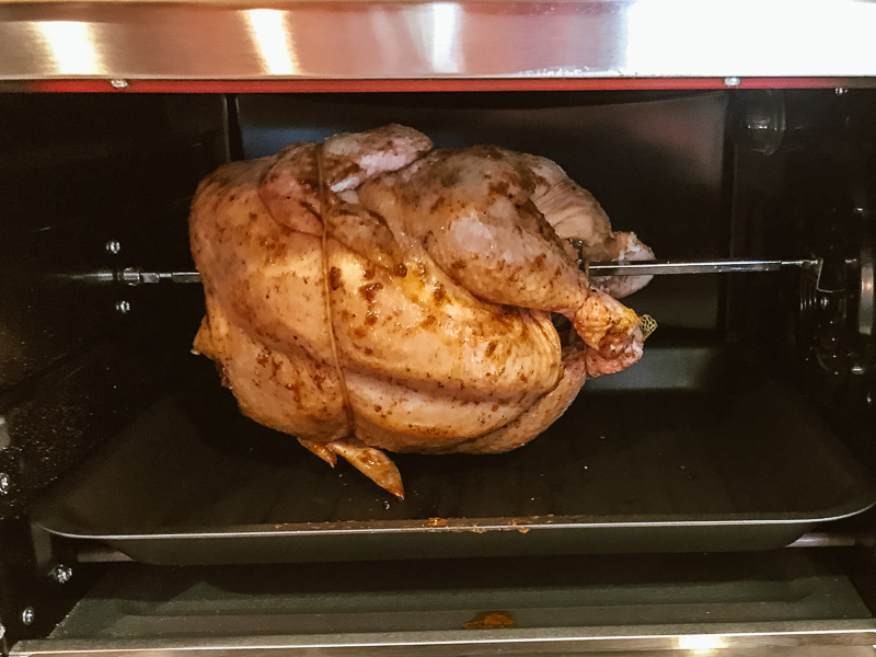 Whole chicken on rotisserie arm inside air fryer toaster oven.