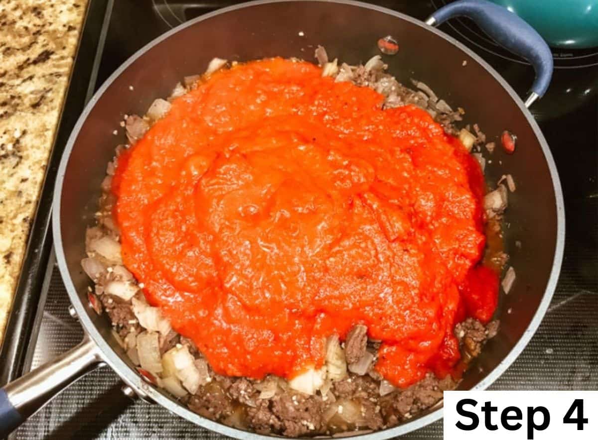 Marinara sauced poured over cooked ground beef and onions in a pan.