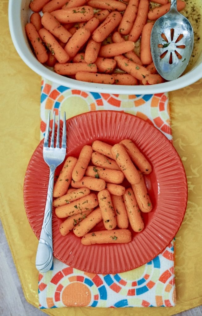 A plate of carrots below a baking dish of buttered carrots with a spoon inside the dish.