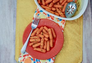 A red plate filled with buttered carrots and a fork propped on top.
