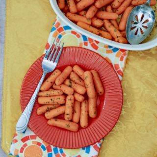 A red plate filled with buttered carrots and a fork propped on top.