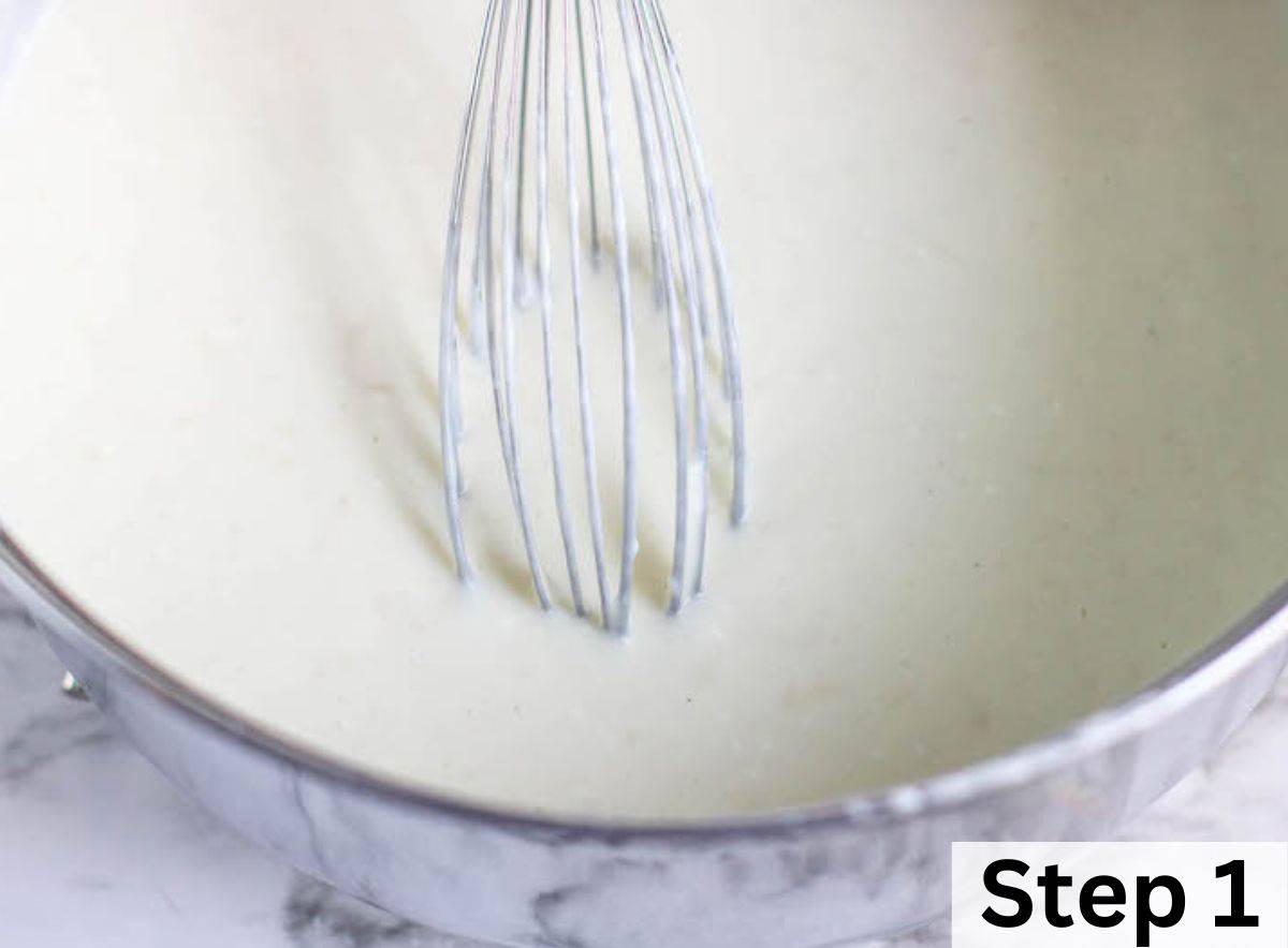 A white cream sauce in a large pot with a whisk in the middle.