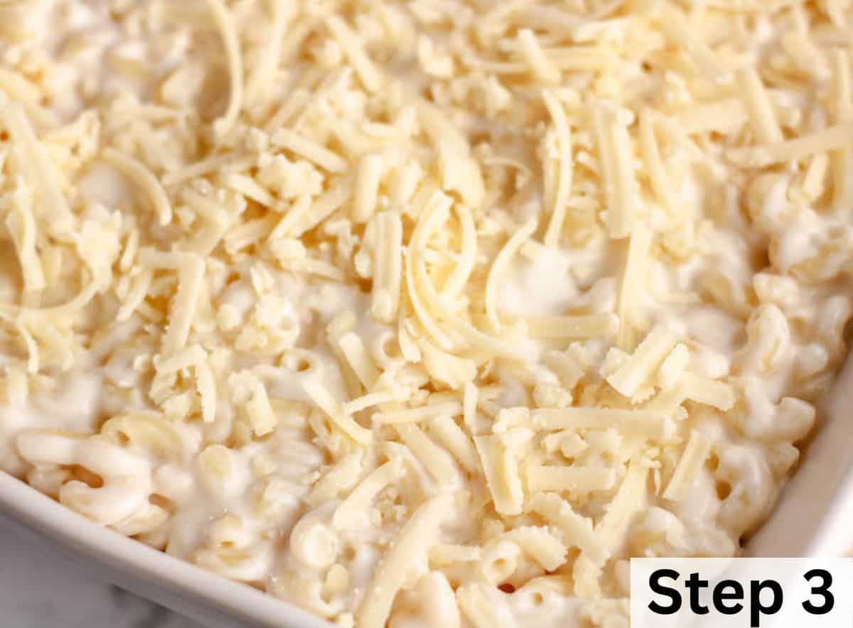 A white casserole dish filled with macaroni and cheese and topped with shredded white cheddar cheese.