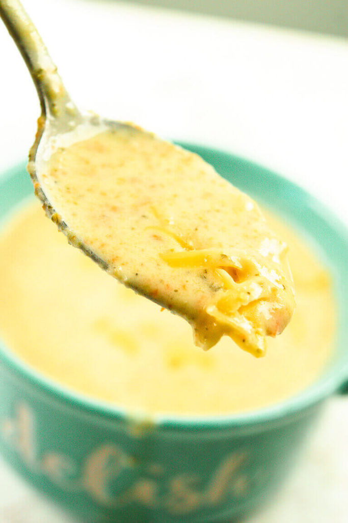 A spoonful of broccoli cheese soup over a bowl of the soup.