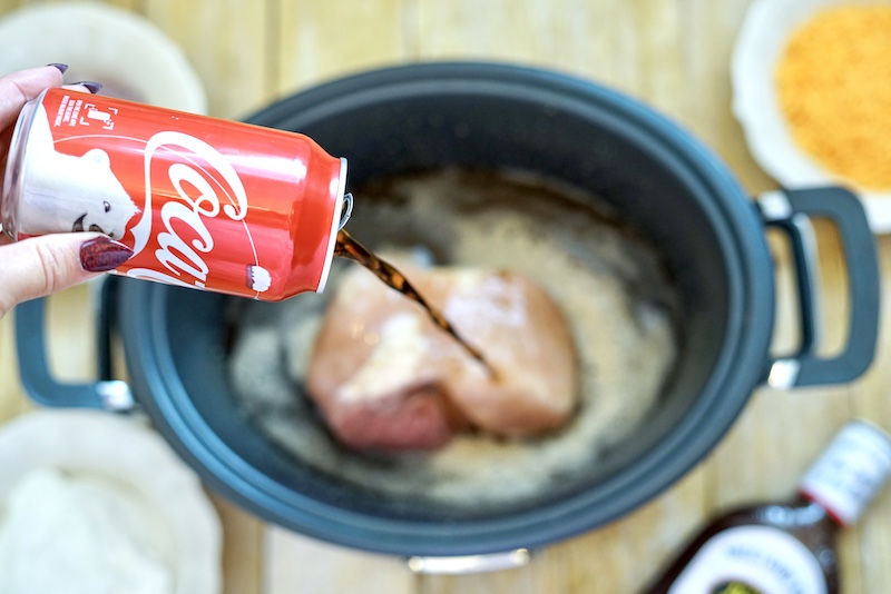 A can of CocaCola pouring over pork roast in crockpot.