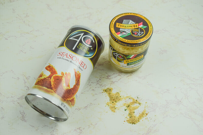 A container of bread crumbs on it's side next to a jar of parmesan cheese.
