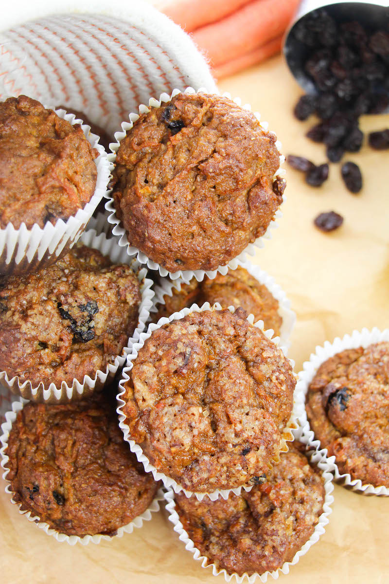 Overhead shot of pile of morning glory muffins next to a cup of raisons spilling out onto the counter.