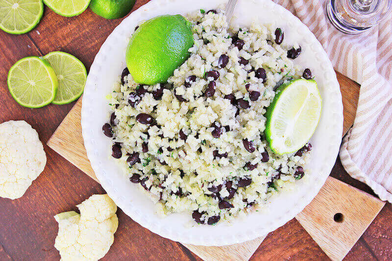 Over head shot of instant to cauliflower rice in a white dish topped with lime wedges.