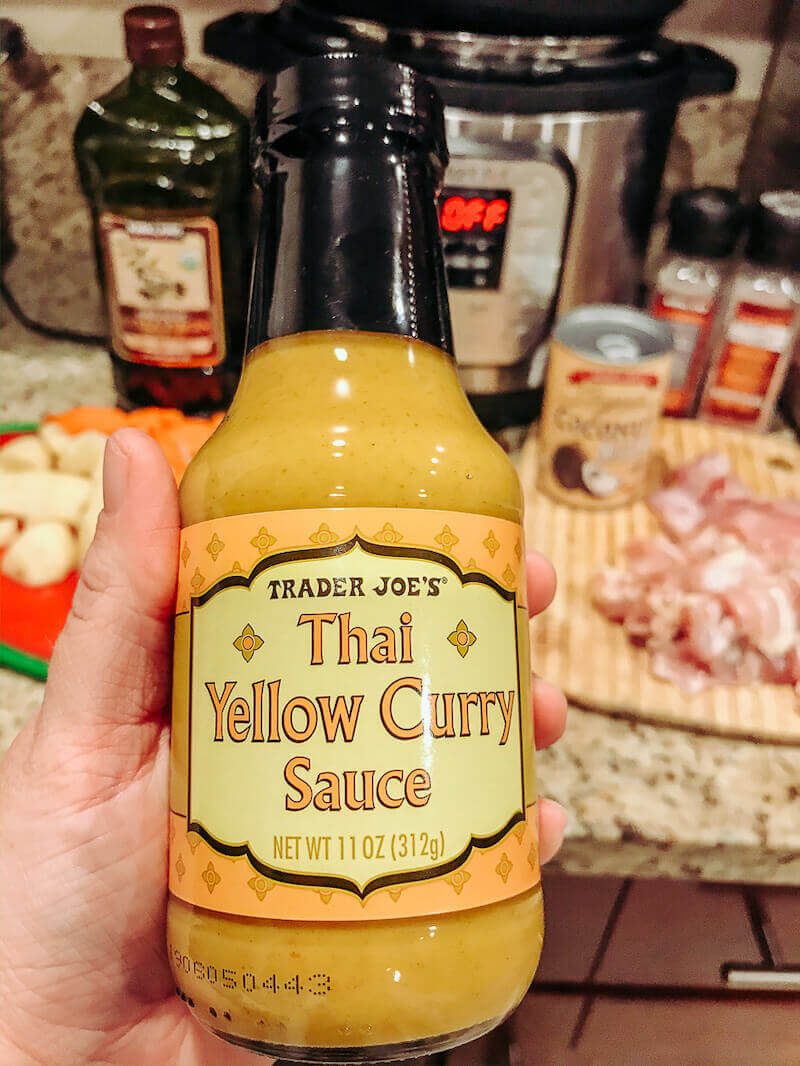 A hand holding a bottle of yellow curry sauce.