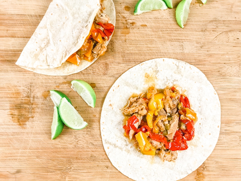 A cutting board with two chicken fajitas - one open and one closed.