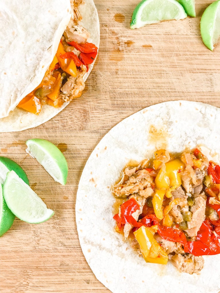 A wooden cutting board filled with two chicken fajita and piles of lime wedges.