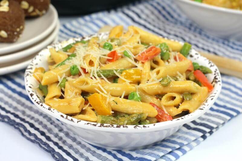 A white bowl filled with chicken pasta with asparagus and peas.