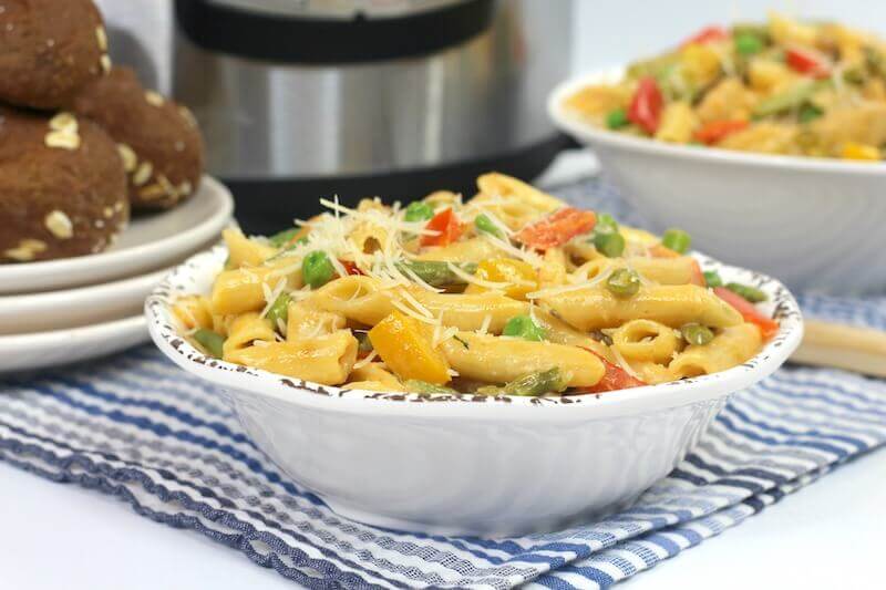 Side view of a bowl of chicken pasta in front of an instant pot.