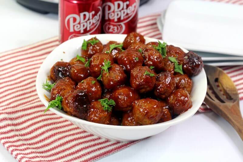A white bowl fowl of cocktail meatballs in front of two cans of Dr. Pepper.