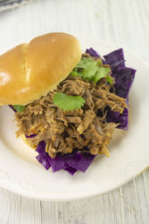 A pulled pork sandwich with top bun sliding off to the side.