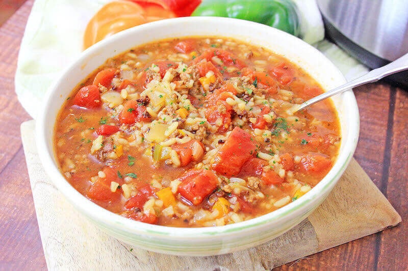 White bowl of stuffed pepper soup on a wooden surface.