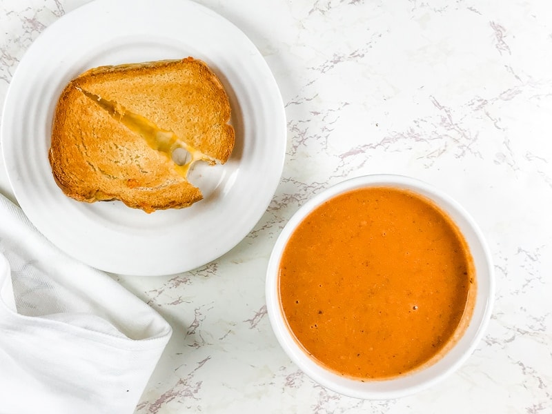A bowl of tomato soup next to a grilled cheese cut in half.