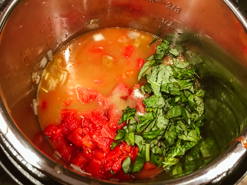 Pot filled with broth, tomatoes, and basil.