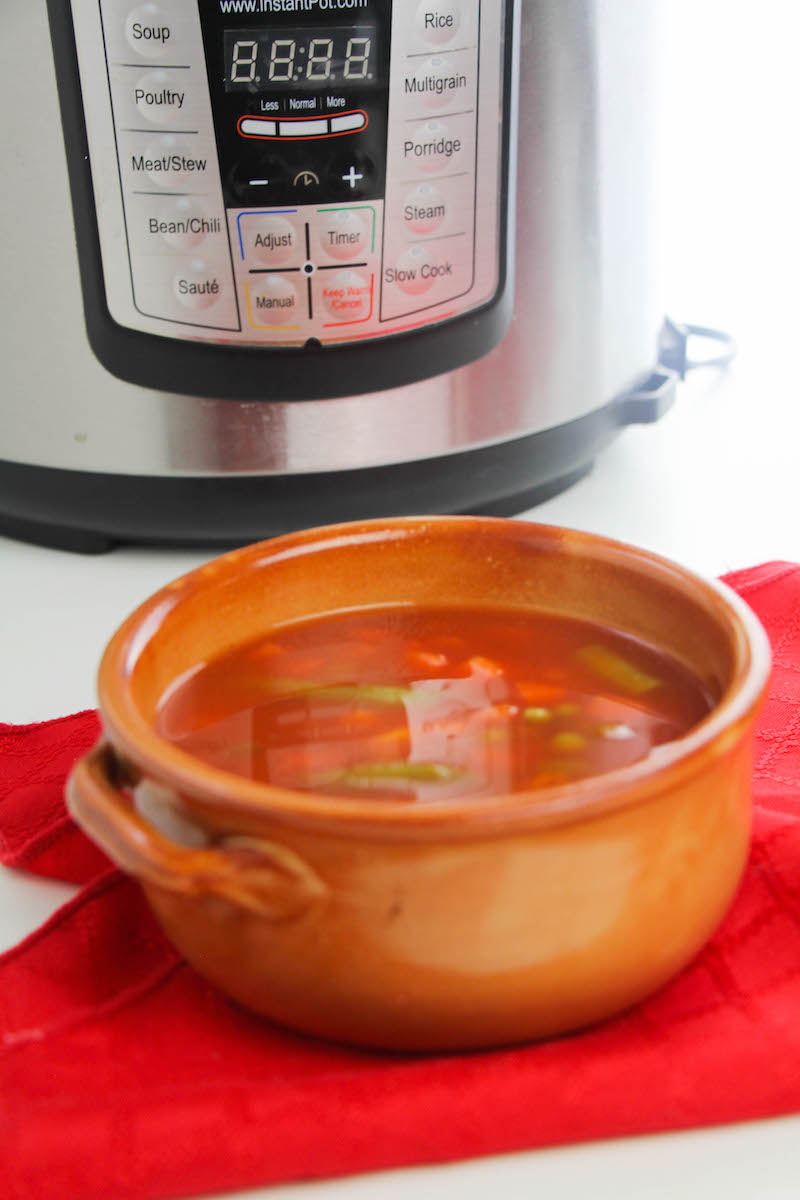 Orange bowl of vegetable soup with instant pot in background.