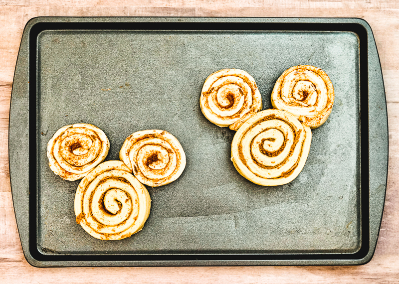 Two unbaked cinnamon rolls shaped like Mickey Mouse.