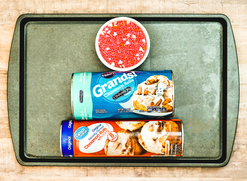 A cookie sheet with two cans of cinnamon rolls and pink sprinkles.