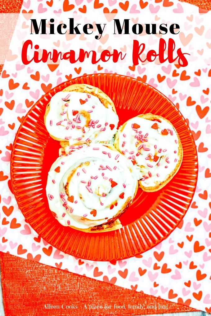 Valentine cinnamon rolls on a red plate on top of heart printed paper.