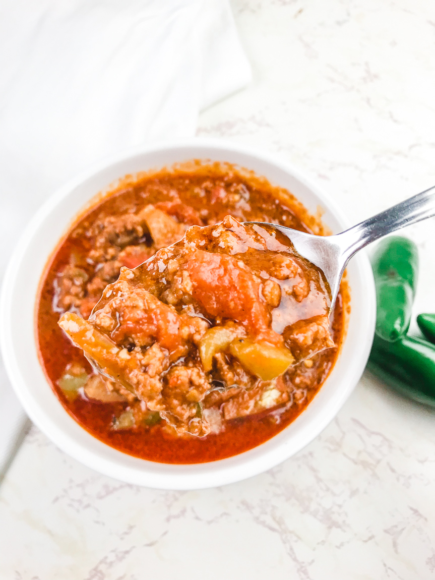 A spoonful of chili above a bowl of chili.