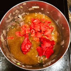 Tomatoes and spices added into pot of cooked beef and peppers.