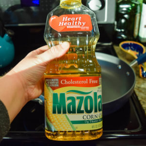 A bottle of corn oil being held in front of hot skillet.