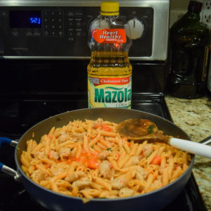 Pasta fully cooked inside of skillet next to bottle of Mazola Corn Oil.