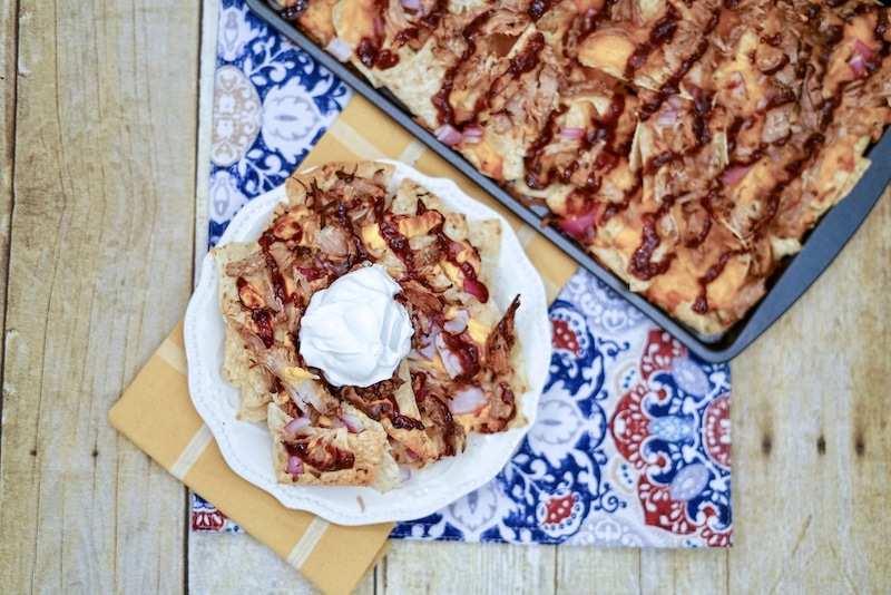 A white plate of pulled pork nachos next to a baking sheet of nachos.