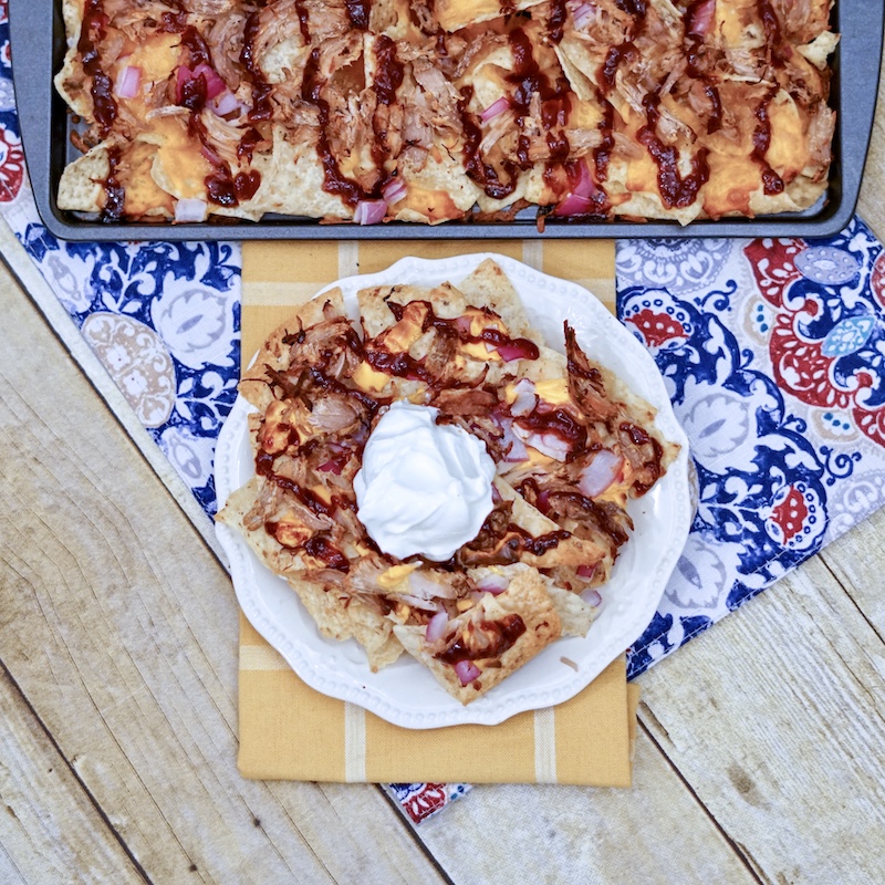 A plate filled with pulled pork nachos drizzled in bbq sauce.