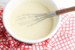 Pancakes batter in a white bowl with a whisk in the bowl.