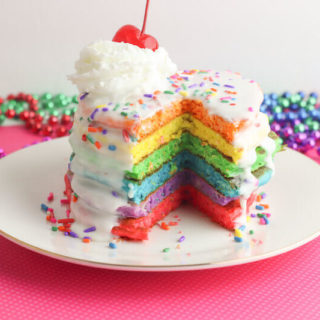 A stack of rainbow colored pancakes with a triangle cut out of them, showing the colors.