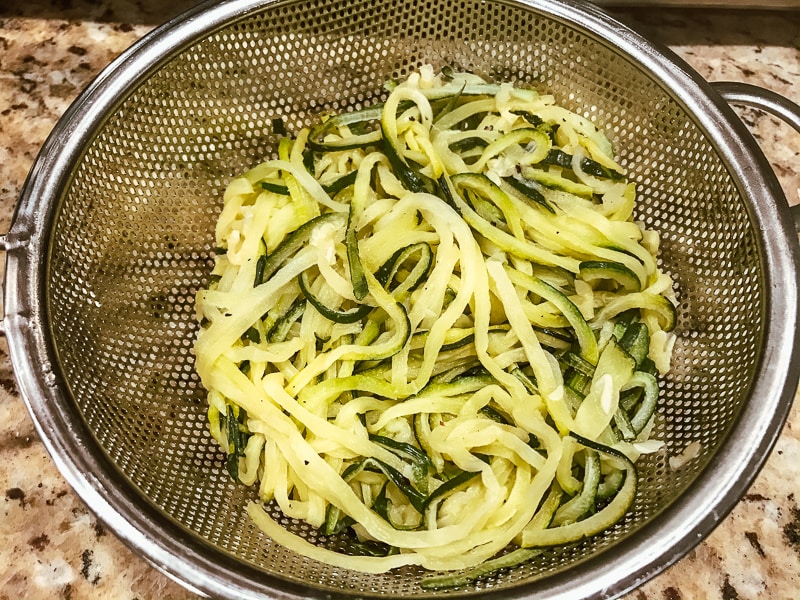Zucchini noodles draining in a mesh sieve.