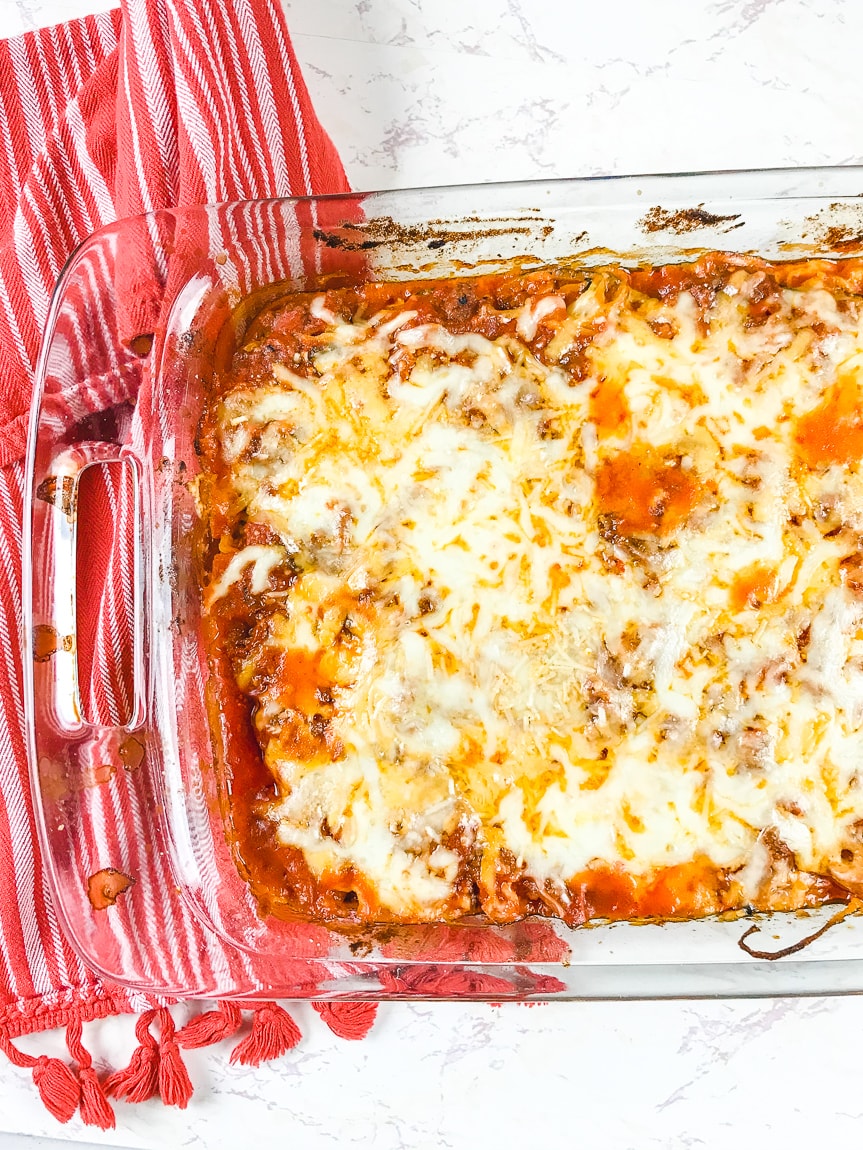 A casserole dish full of zucchini baked ziti next to a red striped towel.