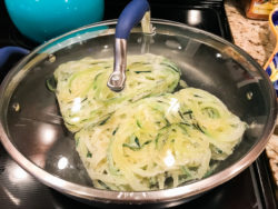A covered skillet with frozen zucchini spirals.