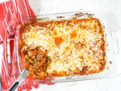A casserole dish with a pasta spoon filed with a scoop of zucchini baked ziti.