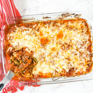 A casserole dish with a pasta spoon filed with a scoop of zucchini baked ziti.