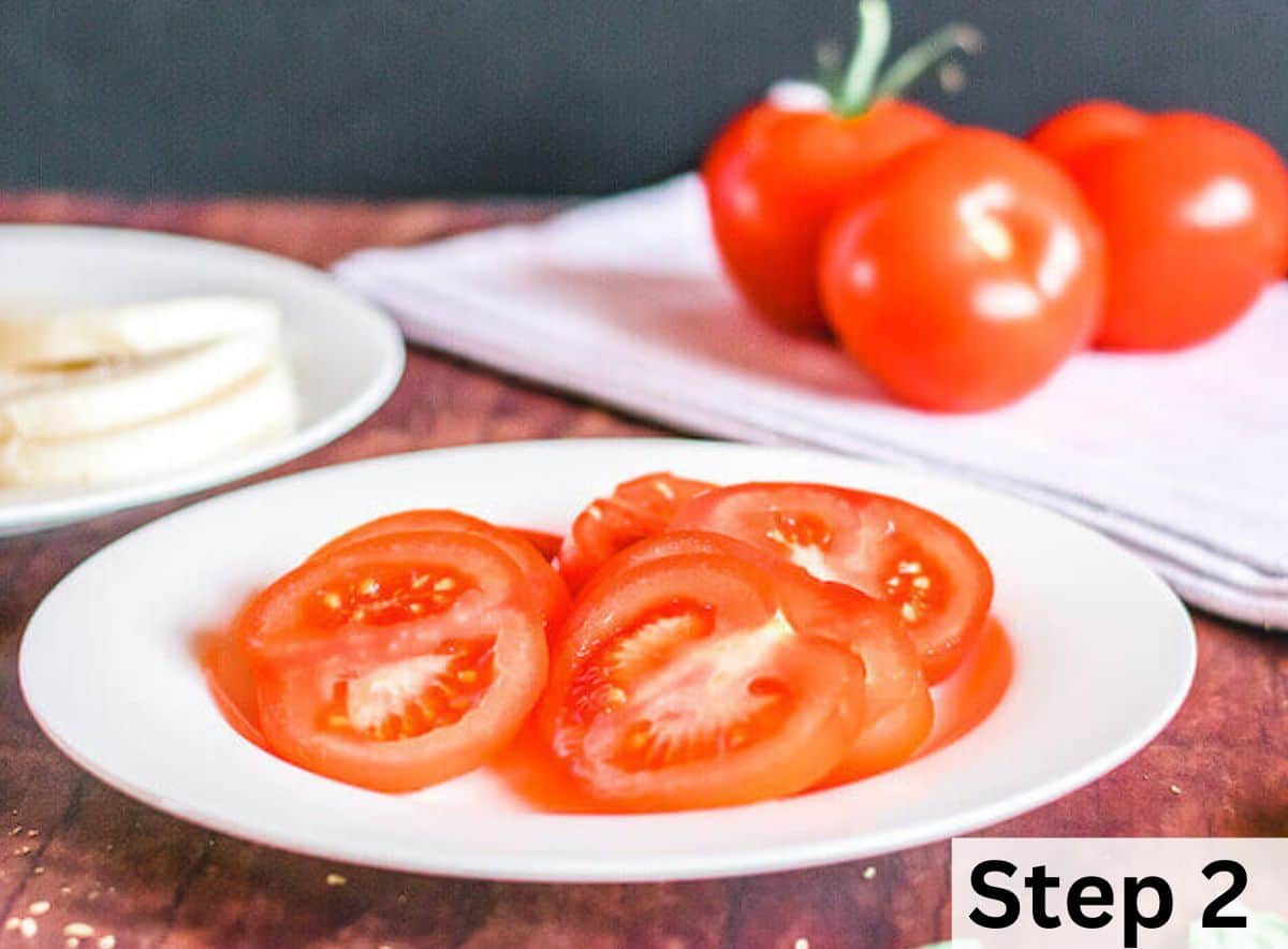 Sliced tomatoes on a white plate in front of three whole tomatoes. 
