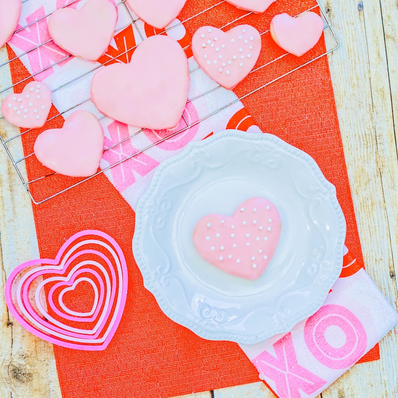 A red place covered in pink heart shaped sugar cookies with pink icing.