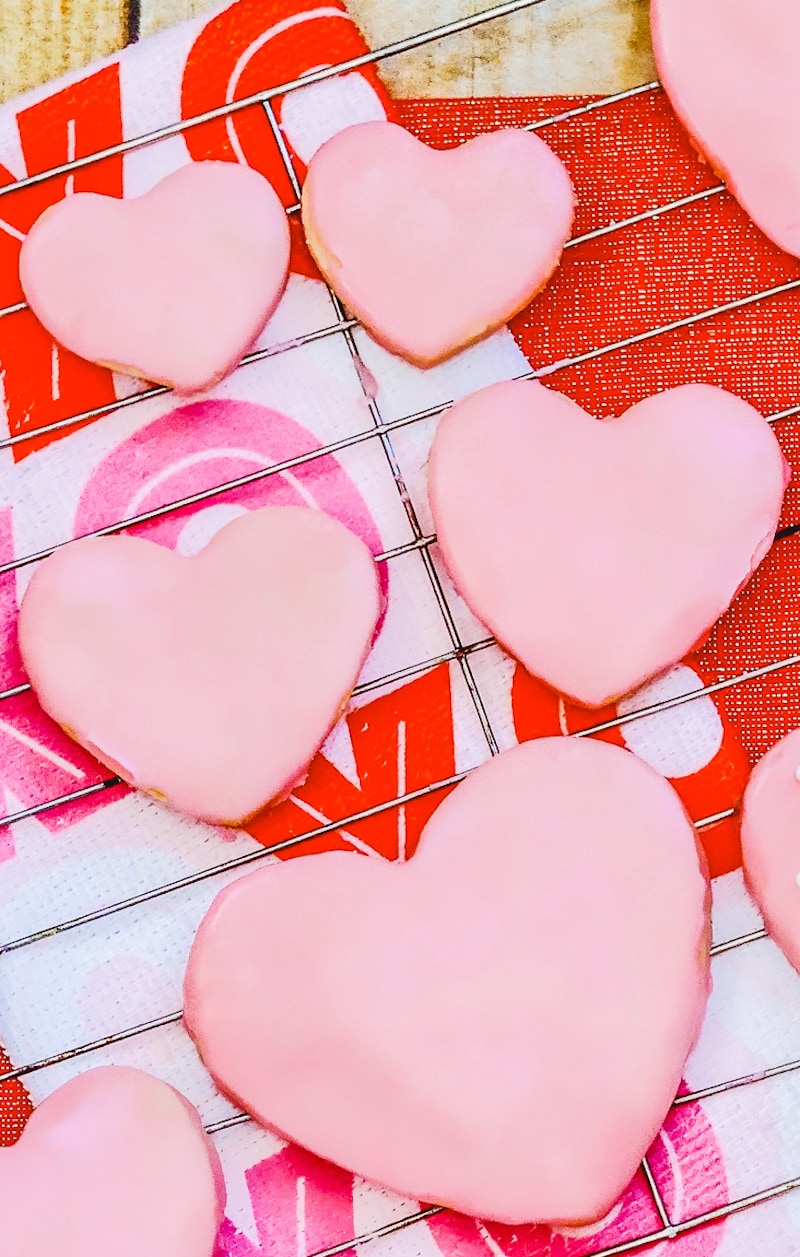 Big and small heart shaped cookies with pink icing on a cooling rack.